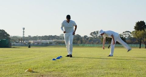Cricket teammates practicing footwork and agility drills with cones on sunny green field