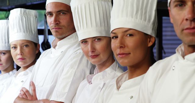 Chefs in professional uniforms standing together in a line in a commercial kitchen. This image can be used for articles related to culinary careers, teamwork in the kitchen, restaurant promotions, or showcasing professional kitchen staff.