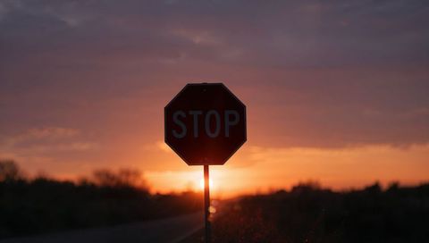 Silhouetting stop sign at sunset creating dramatic backlit roadside scene with gradient sky