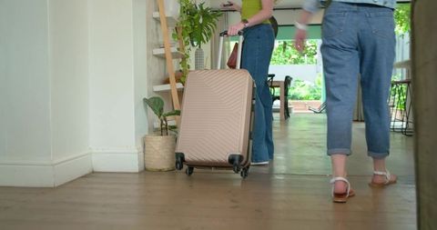 Diverse friends pulling rose-gold suitcase through bright home interior weekend getaway