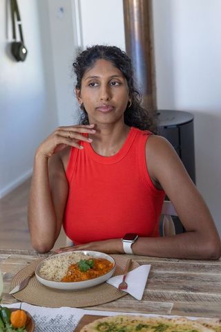 Asian woman sitting at dining table in sleeveless red top looking right at curry bowl