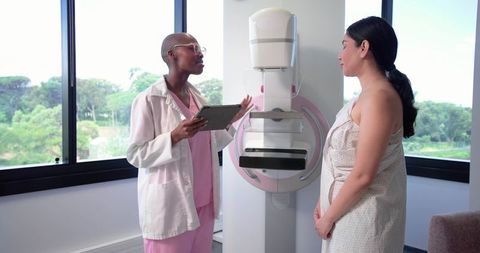 Clinician explaining mammogram procedure to patient in bright clinic using tablet