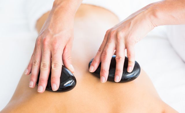 Cropped image of masseur giving hot stone massage on woman back at spa