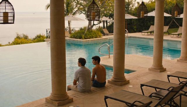 Two teenage friends sitting at infinity pool overlooking ocean on luxury resort terrace