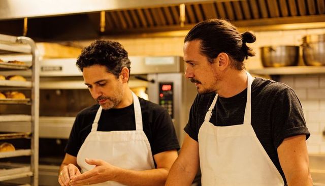 Bakers collaborating in bakery kitchen shaping dough and inspecting bread racks