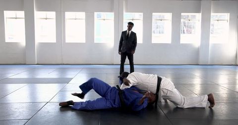 Martial arts competitors in intense grappling match under referee supervision