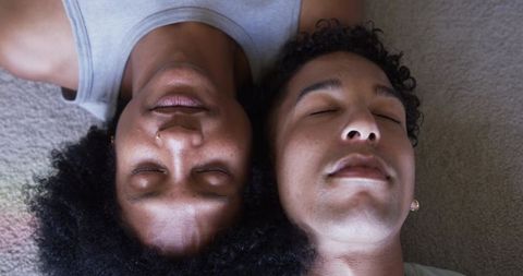 Lying on carpet, same-sex couple sharing quiet intimate moment with single tear, closeup