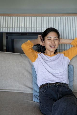 Asian woman relaxing comfortably on gray sofa at home