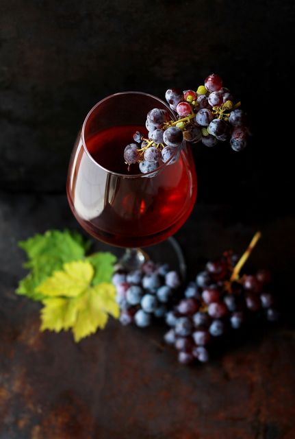 This image features a glass of red wine adorned with grape clusters and leaves against a dark background. It captures the essence of sophistication and elegance associated with wine. Ideal for use in advertisements, wine promotions, restaurant menus, websites, or any marketing material related to wine and fine dining. The rich colors and composition highlight the beauty of both the wine and grapes, appealing to wine enthusiasts and connoisseurs.