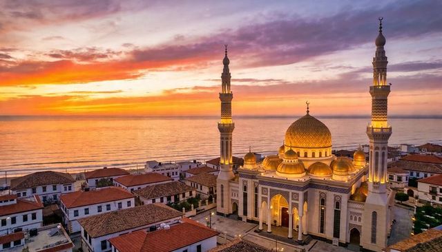 Golden coastal mosque at sunset with twin minarets, ornate domes and terracotta rooftops