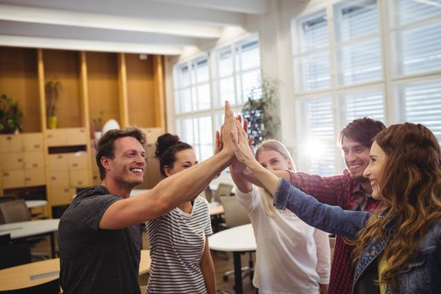 Group of business executives giving high five in office, expressing teamwork and success. Ideal for use in corporate presentations, team-building materials, motivational posters, and business websites to illustrate collaboration, unity, and a positive work environment.