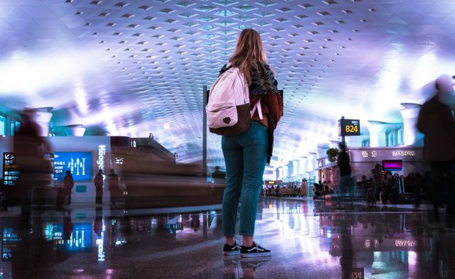 Young woman stands in illuminated modern airport terminal, waiting for departure. Useful for travel-related websites, blogs on airport experiences, or articles about solo adventure tips.
