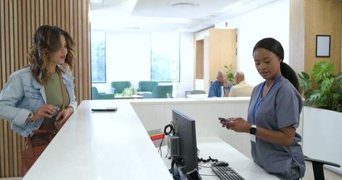 Clinic receptionist using smartphone while patient waiting at bright medical front desk
