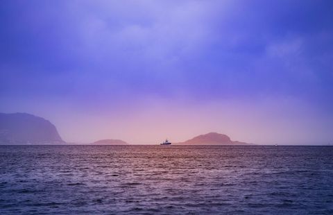 Fishing Vessel Sailing Past Distant Islands at Pastel Sunset Over Calm Ocean Horizon