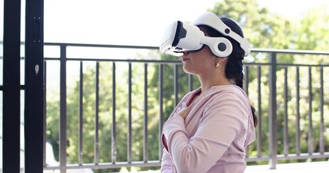 Woman wearing white vr headset on balcony experiencing immersive virtual relaxation