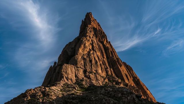 Jagged granite spire catching golden light with wispy cirrus clouds over foothills