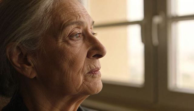 Senior woman gazing through window, thoughtful profile portrait with natural light