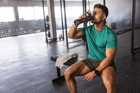 Fit asian man drinking protein shake on gym bench after intense strength training session