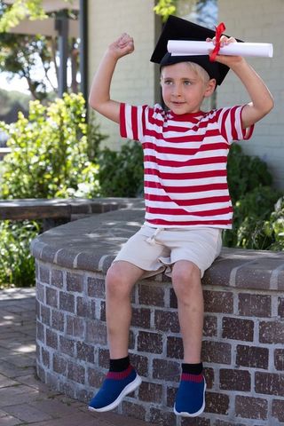 Young graduate celebrating with diploma and mortarboard sitting on brick planter outdoors