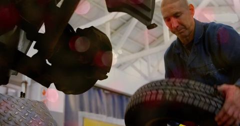 Mechanic fitting spare wheel under raised vehicle on garage lift focusing on wheel hub
