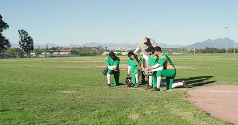 Baseball team kneeling and listening to coach on sunny diamond during pregame practice