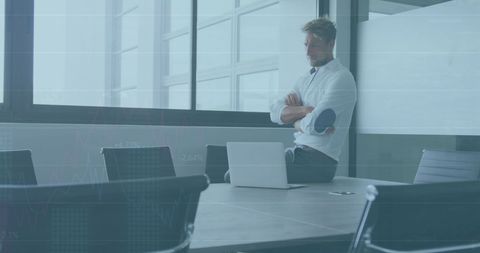 Thoughtful Businessman Leaning Against Office Window with Laptop
