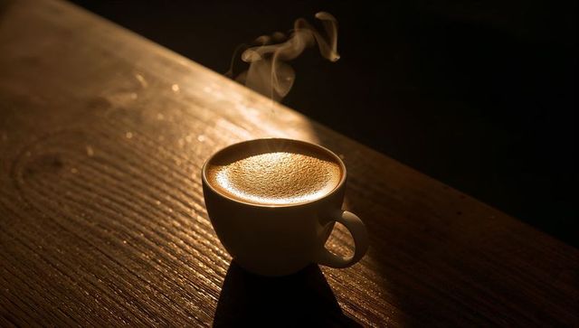 Steaming cup of espresso with golden crema on rustic wooden table, warm cozy morning