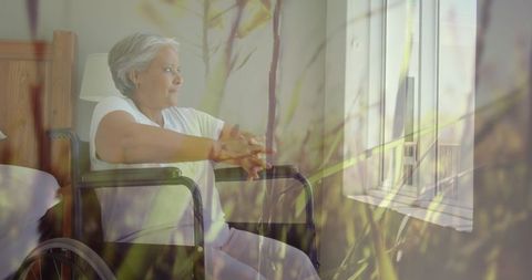 Pensive senior woman in wheelchair daydreaming at window with nature overlay