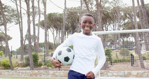 Energetic Boy Playing Soccer on Park Field by Woodland Goal