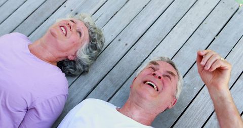 Senior Couple Relaxing Happily on Wooden Deck with Joyful Expressions