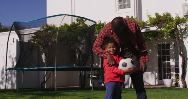 Portrait of happy african american man and his son holding football in garden. Spending quality time at home.