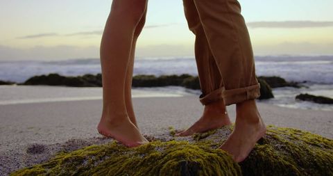 Romantic barefoot couple standing on sunrise beach rock