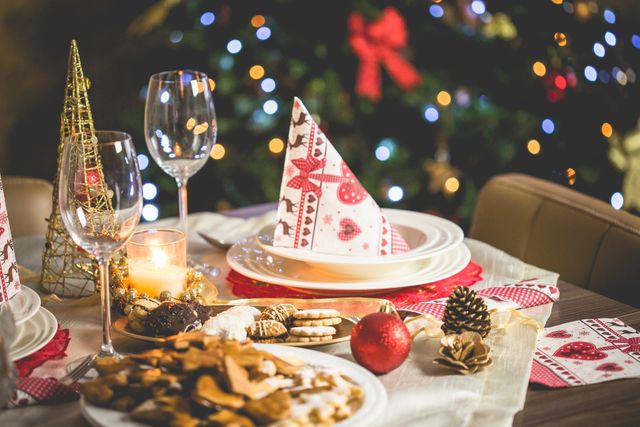 Elegant Christmas-themed table arranged with festive decorations, plates, and glasses. Christmas tree with lights in background, adding warmth and atmosphere. Ideal for holiday blogs, festive menu promotions, and seasonal greeting cards.