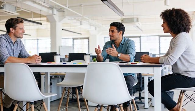 Collaborating coworkers brainstorming around table in modern open-plan office with coffee