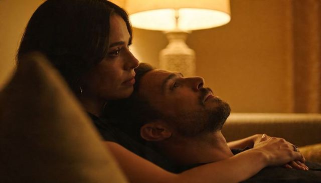 Couple sharing intimate sofa embrace at night, woman cradling man's head in warm lamp glow