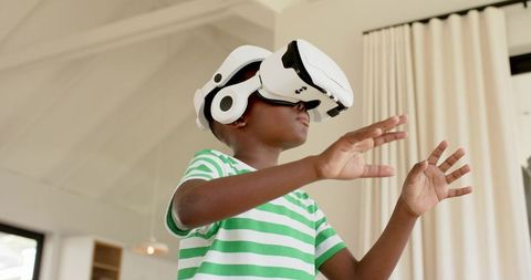 Young boy exploring virtual reality in sunlit living room wearing headset and headphones