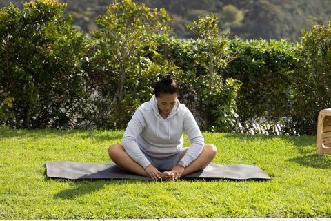 Asian woman practicing seated butterfly stretch on yoga mat outdoors in sunny garden