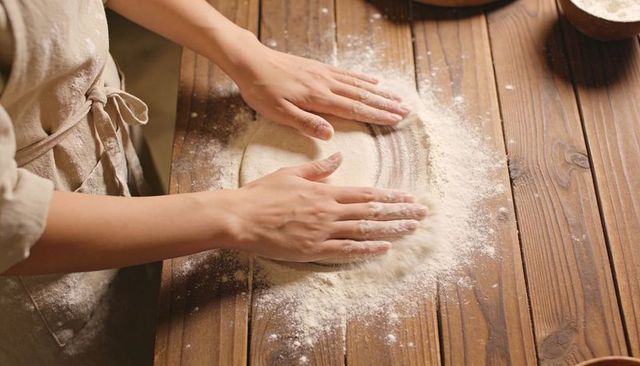 Baker shaping rustic dough on wooden countertop, kneading with flour-dusted linen apron