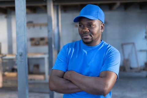 Confident african american craftsman standing with arms crossed in industrial workshop