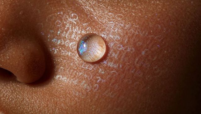 Macro cheek revealing skin pores and magnifying water droplet with iridescent shimmer