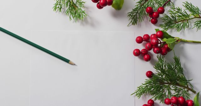 Blank paper lying amid festive Christmas decorations such as red berries and pine branches, paired with a green pencil. Ideal for holiday greeting cards, festive invitations, record holiday memories or to encourage Christmas crafts and creativity.