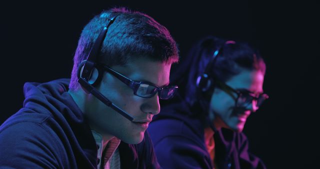 Focused gamers wear headsets in a dimly lit room. They are deeply engaged in an intense gaming session, highlighting the popularity of esports.