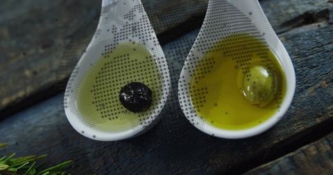 Ceramic spoons with black and green olives in olive oil on rustic board