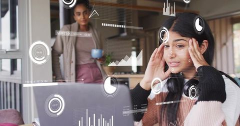 Stressed teen studying on laptop with headphones and data hud overlays in home office