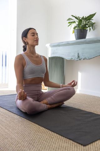 Woman meditating at home on yoga mat practicing mindfulness and relaxation