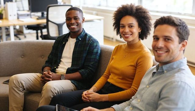 Smiling diverse team sitting on sofa in modern office lounge using tablet for collaboration