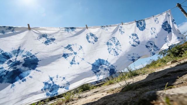Hanging indigo tie-dye sheet billowing on clothesline over sunlit rocky hillside