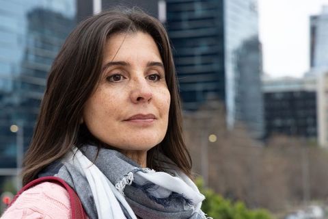 Contemplative middle-aged woman standing on urban sidewalk wearing scarf and pink sweater