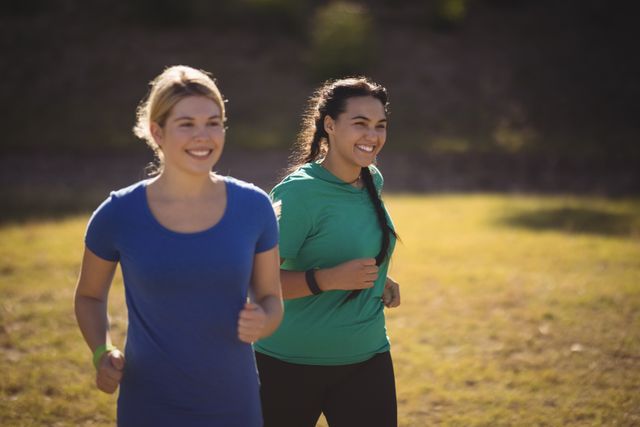 Two women are running on grass during a boot camp, smiling and enjoying the exercise. This image can be used for promoting fitness programs, outdoor activities, team-building events, and healthy lifestyle campaigns. It highlights the joy of exercising with friends and the benefits of staying active.