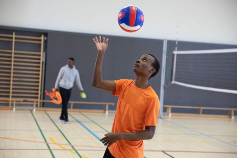 African american teenager tossing volleyball in school gymnasium during practice session